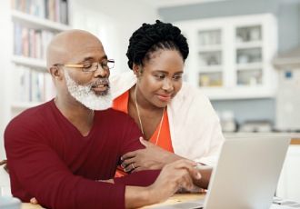 A woman and man look at a laptop computer in their home