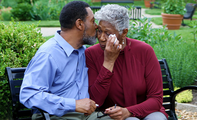 A man comforts his wife as they sit together on a park bench