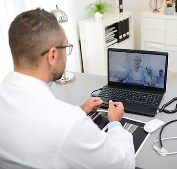 A healthcare professional talks with a woman via videoconference on a laptop